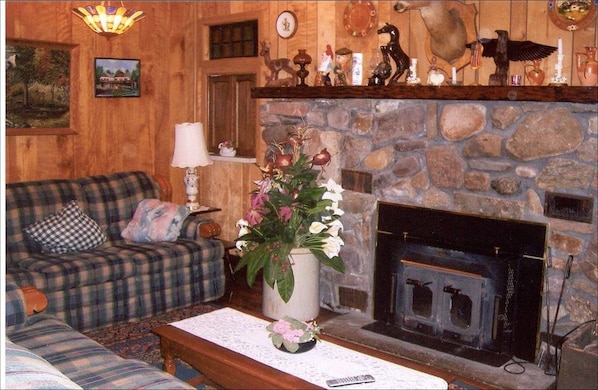 Un salón acogedor con un sofá escocés, una chimenea y varios objetos decorativos en estantes encima de la chimenea.