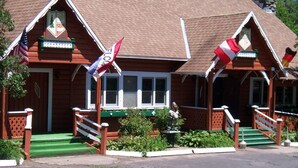 Un chalet en bois avec une pelouse verdoyante, des rampes blanches et des drapeaux.