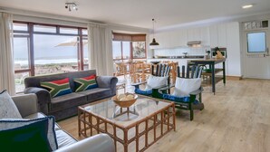 Een ruime woonkamer met een groot raam met uitzicht op zee, een eethoek met houten meubels, en een moderne keuken met witte kastjes.