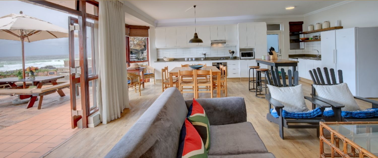 A spacious living area with a sofa, chairs, and a dining table. There is a kitchen area with white cabinets and a dining area with a table and chairs.