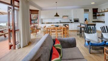 A spacious living area with a sofa, chairs, and a dining table. There is a kitchen area with white cabinets and a dining area with a table and chairs.