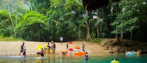 A group of people in a forested area with clear water, some standing and some in rafts.