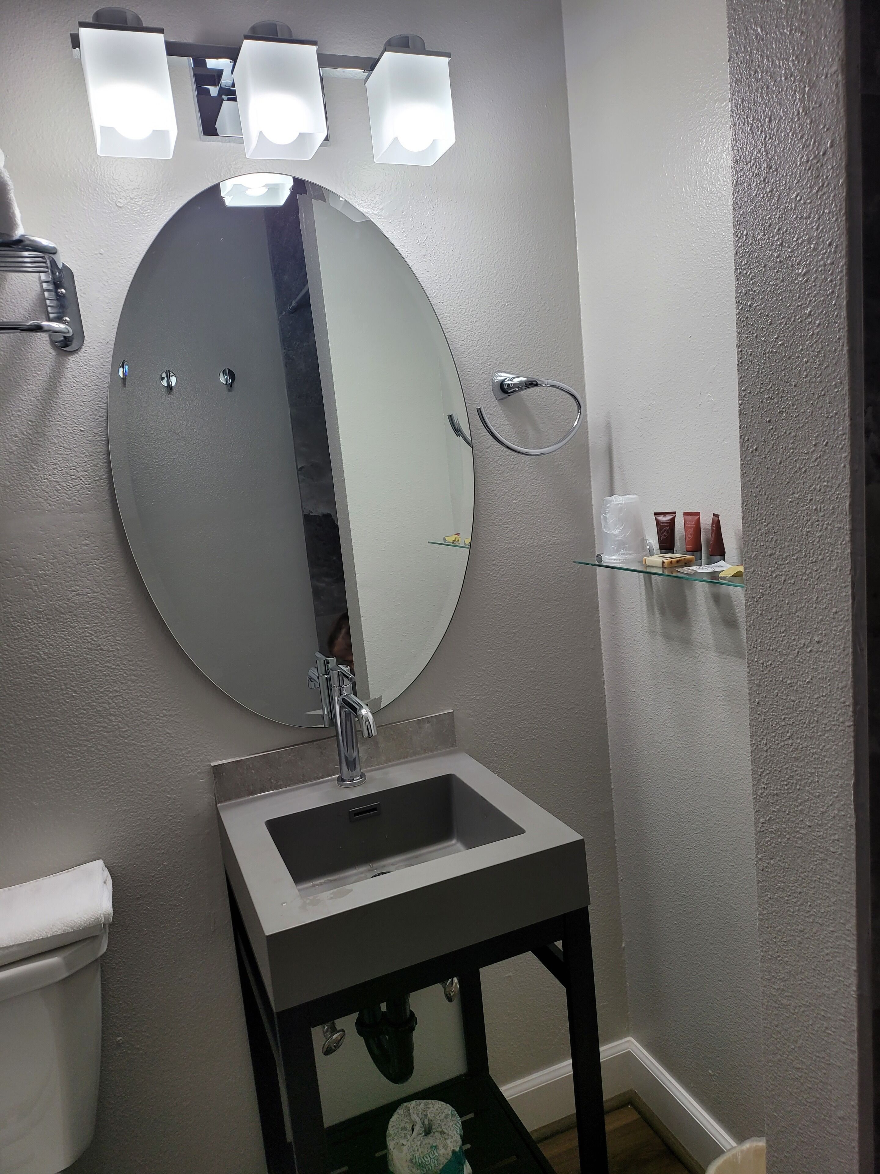 Une salle de bain avec un miroir rond, un lavabo et une étagère contenant des articles de toilette.