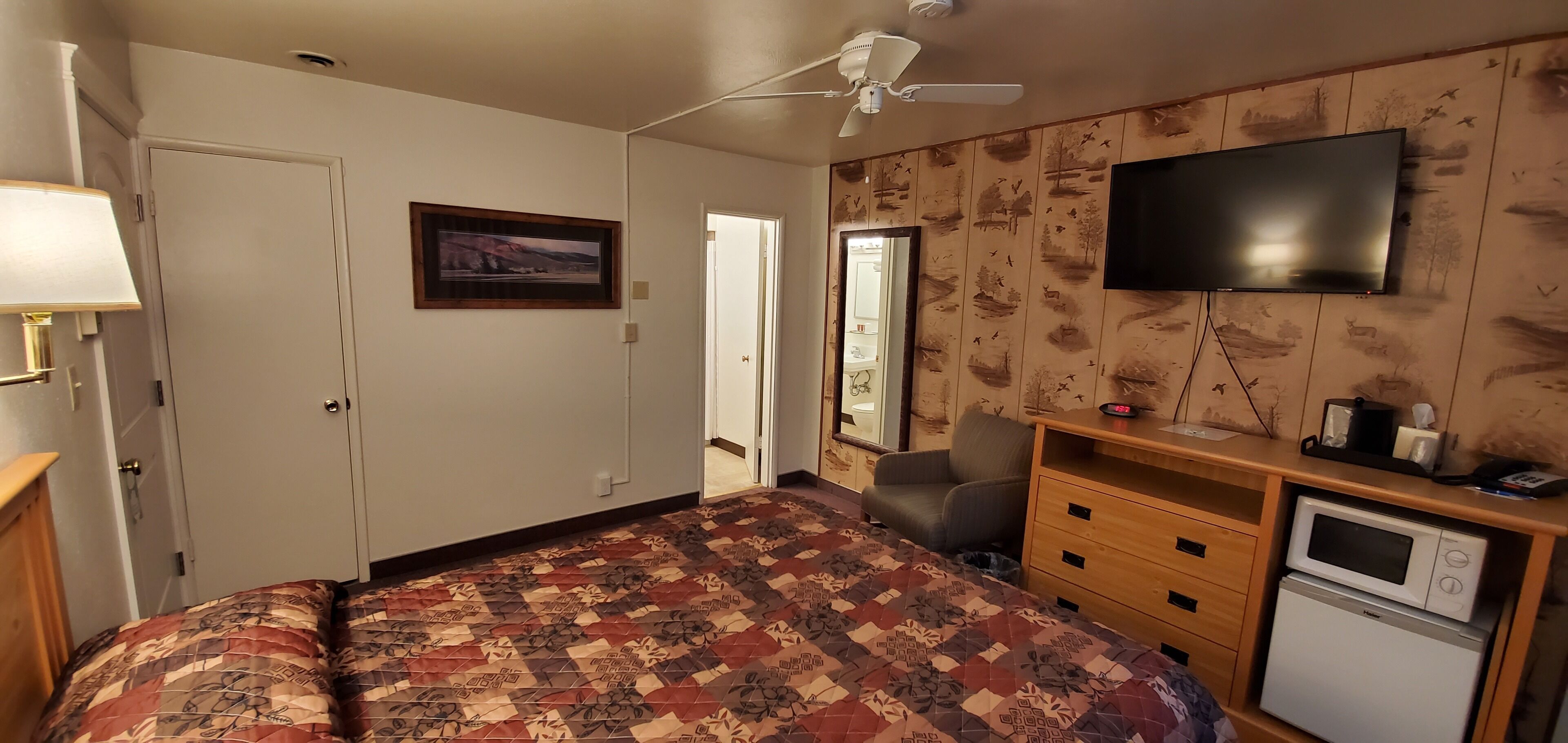 A bedroom with a bed, a desk, a TV, and a microwave.