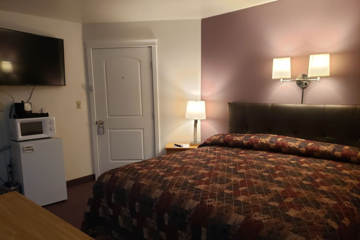 A hotel room with a bed, a microwave, a television, and a nightstand with a lamp.