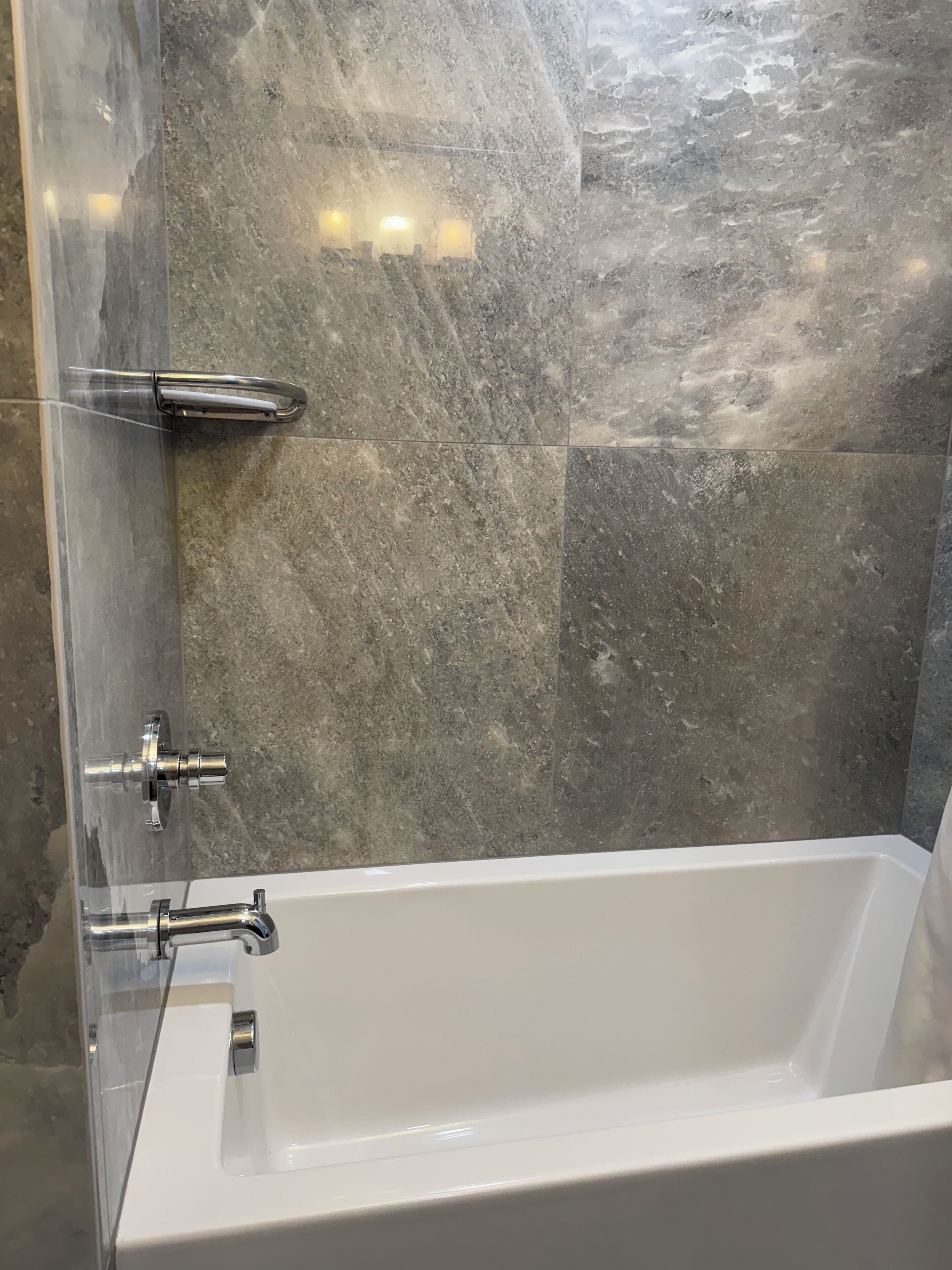 A modern bathroom with a white bathtub, chrome fixtures, and grey marble walls.