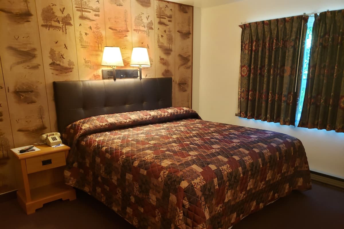 A hotel room with a large bed, two bedside lamps, a telephone, and a nightstand.