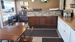 A cozy cafe with a wooden table and chairs, a stone backsplash, and a TV mounted on the wall. - Bridge Street Inn (Baker City)