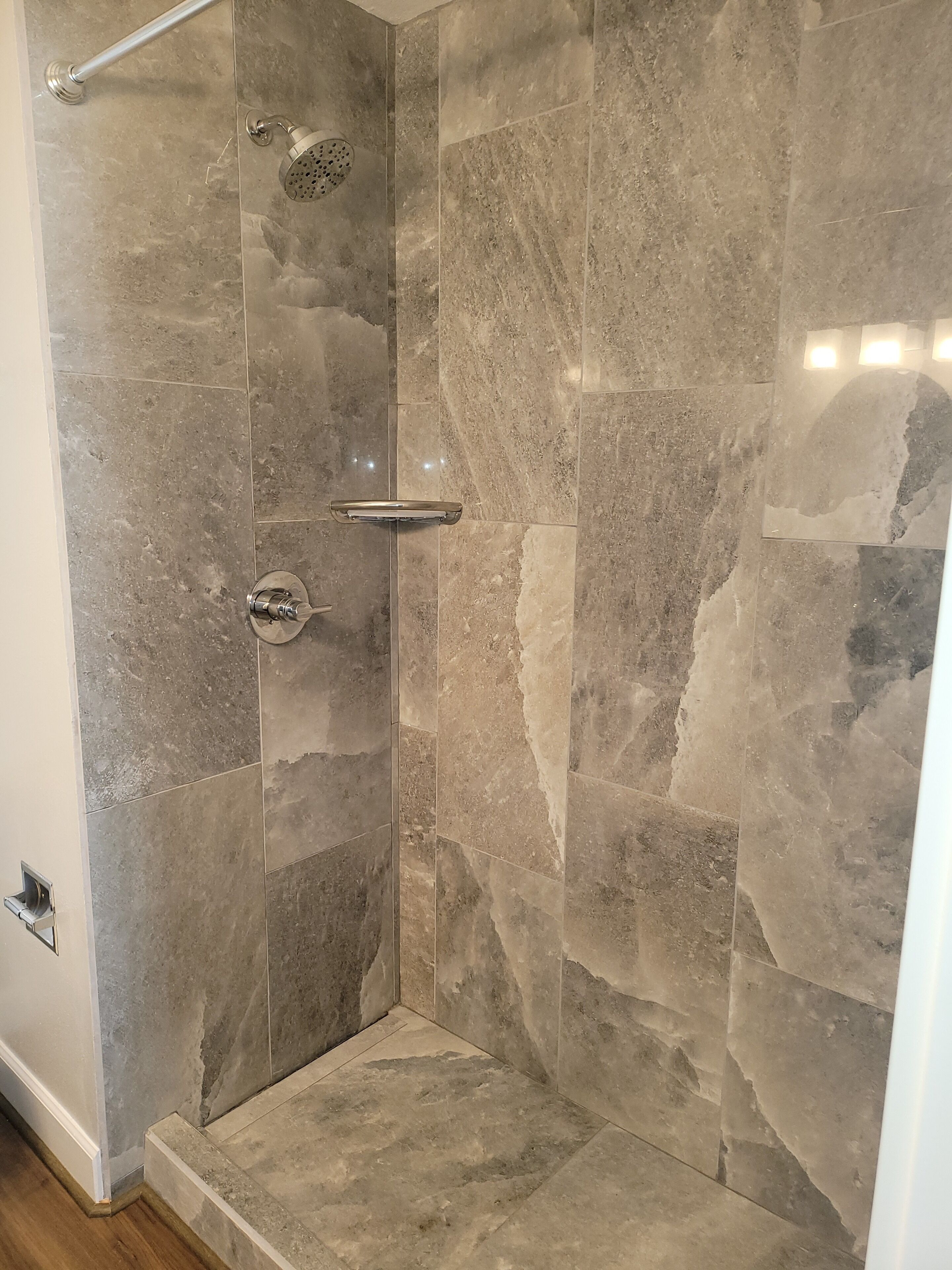 Douche met een glazen deur, een handdouche en bedieningspaneel aan de muur.