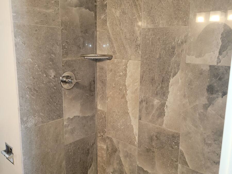 Douche met een glazen deur, een handdouche en bedieningspaneel aan de muur.