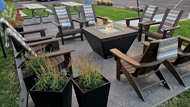 An outdoor seating area with wooden chairs and a central fire feature. - Bridge Street Inn (Baker City)