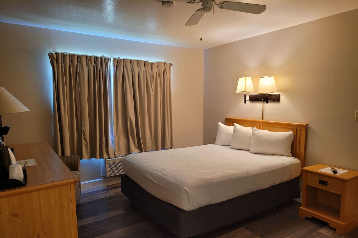 A hotel room with a bed, bedside lamps, a desk, and a ceiling fan.