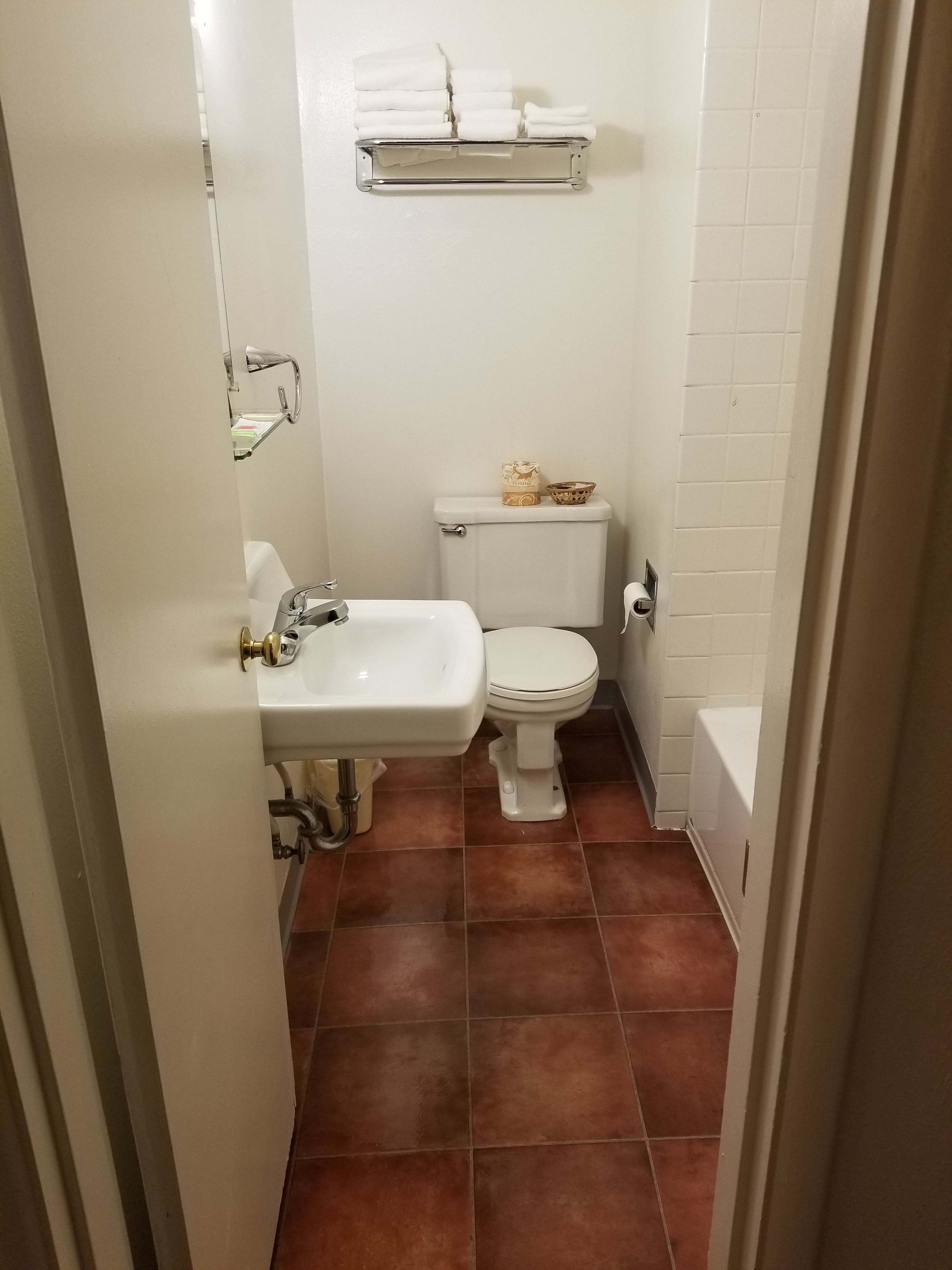 A small bathroom with a white sink, toilet, and a shelf above the toilet holding towels.