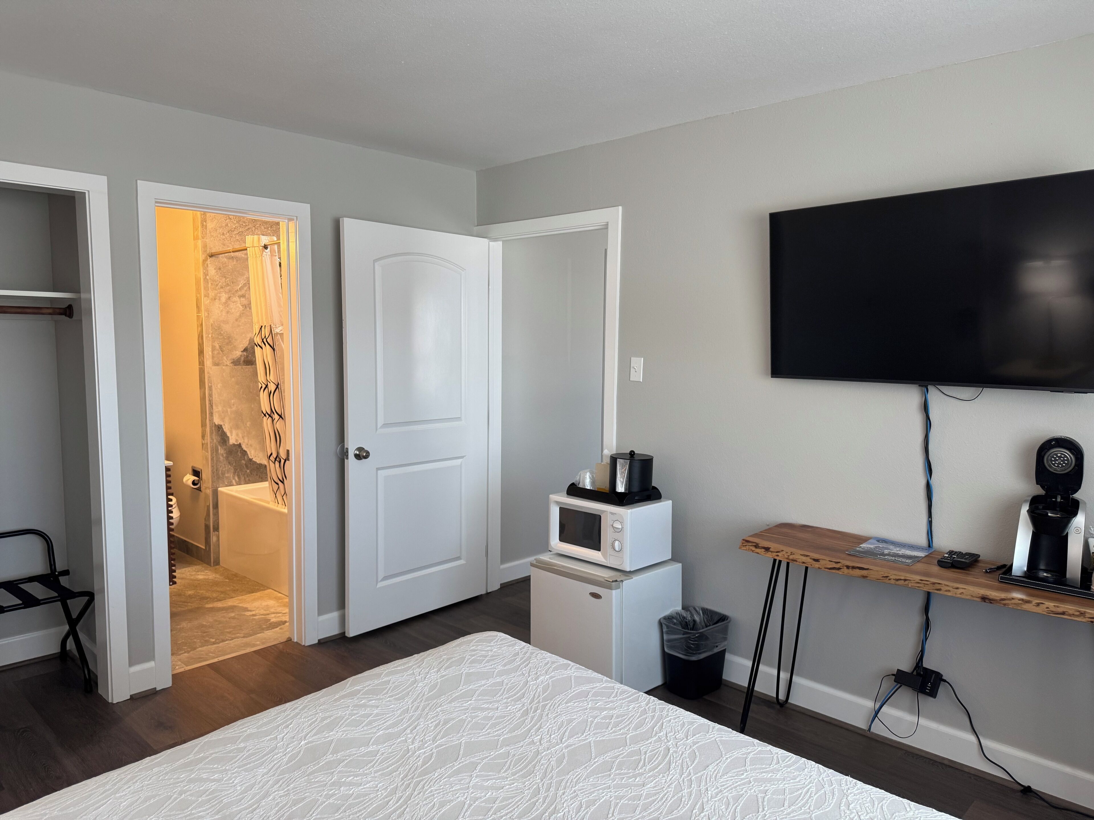 Un dormitorio con una cama, un televisor montado en la pared, un microondas y un refrigerador pequeño.