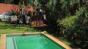 Une piscine rectangulaire dont le bord est recouvert de carreaux, entourée d’une pelouse verdoyante et de diverses plantes.