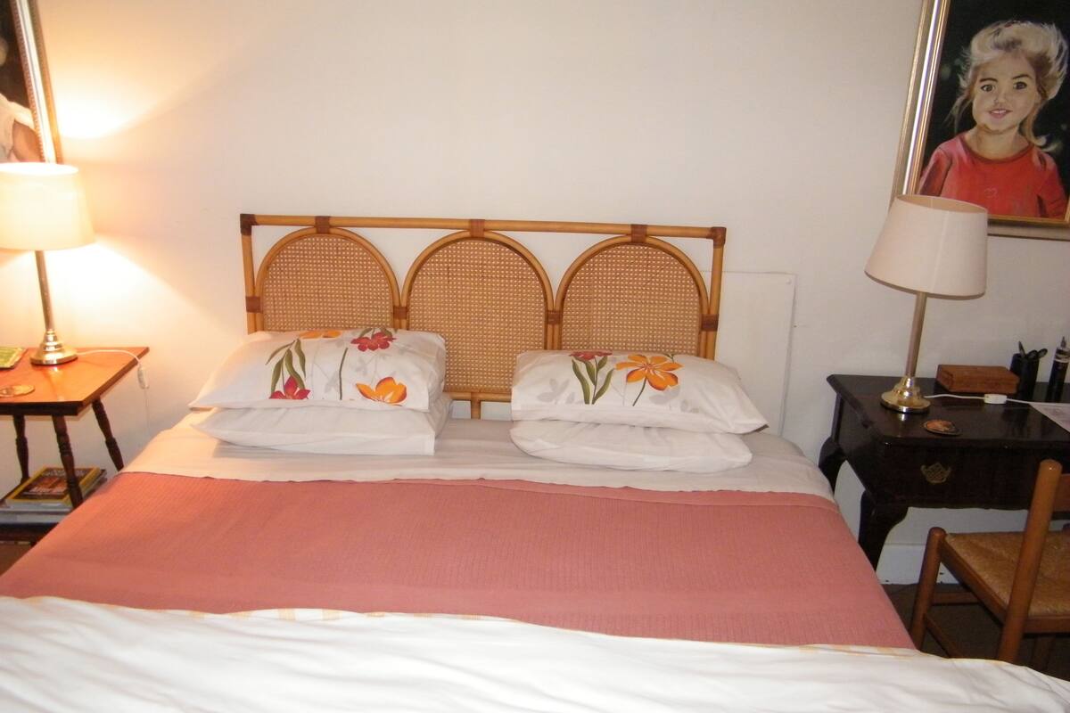 Ein ordentlich bezogenes Bett mit floralen Kissen und einer rosa Tagesdecke in einem Hotelzimmer.