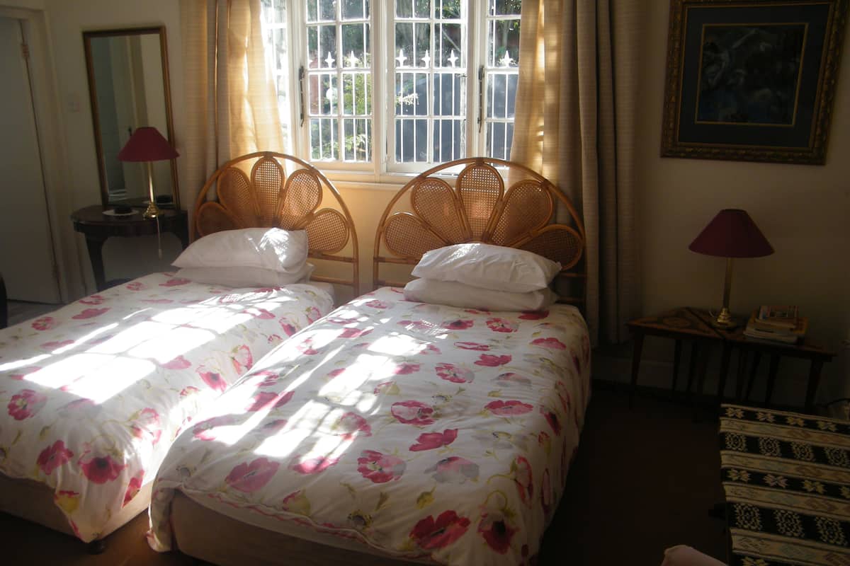 Ein Doppelbett mit floralem Bettbezug, ein Nachttisch mit Lampe und ein Fenster mit Vorhängen.