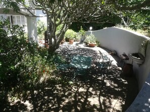 A patio area with a table and chairs, surrounded by potted plants and a white wall. - Valley Guest House (Port Elizabeth)
