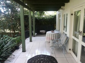 A covered patio with a table and chairs, a tiled floor, and a view of a garden. - Valley Guest House (Port Elizabeth)