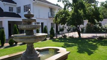 A white building with a multi-tiered fountain in the foreground and a tree to the right.