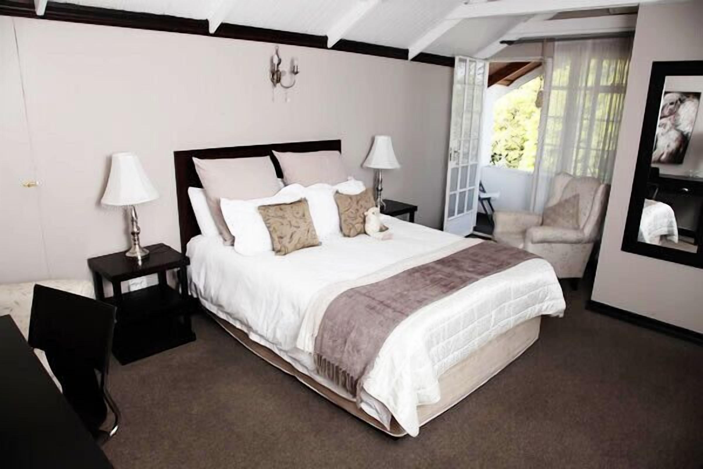 Un dormitorio ordenado con una cama grande, dos mesitas de noche con lámparas, una silla y un espejo en la pared.