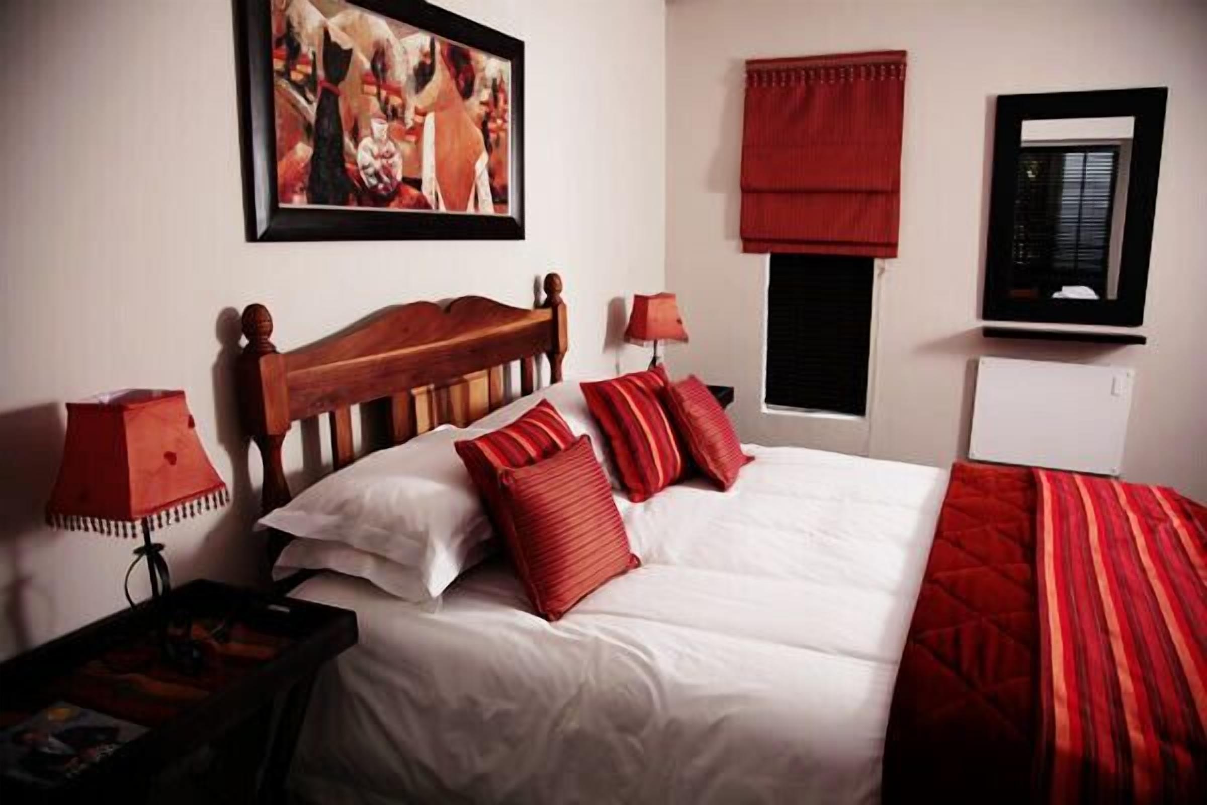 A neatly made bed with white and red bedding, a wooden headboard, and a red lamp on a bedside table.
