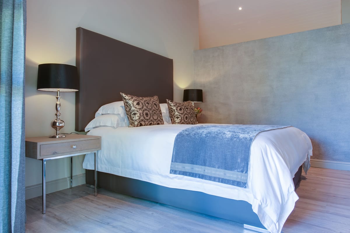 A modern bedroom with a large bed, two bedside tables with lamps, patterned pillows, and a blue accent on the bedspread.
