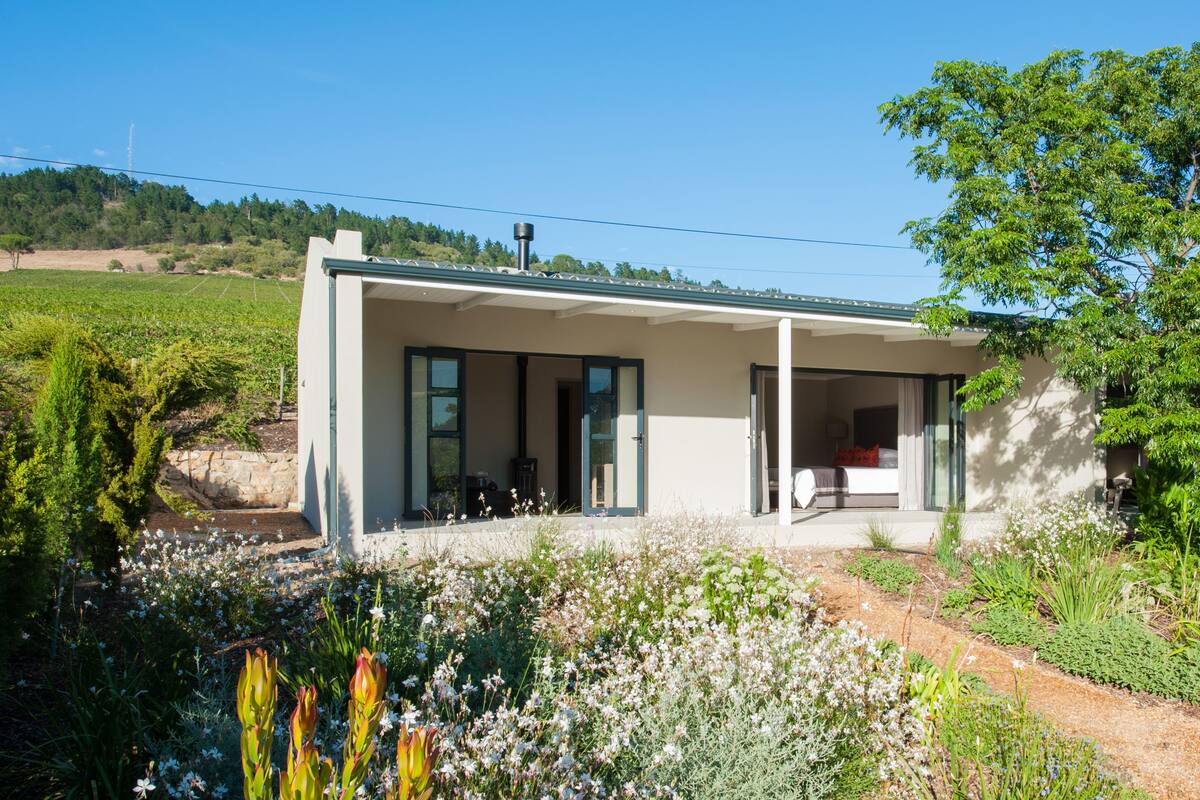 A modern house with a large glass door, a covered porch, and a garden with various plants and flowers.