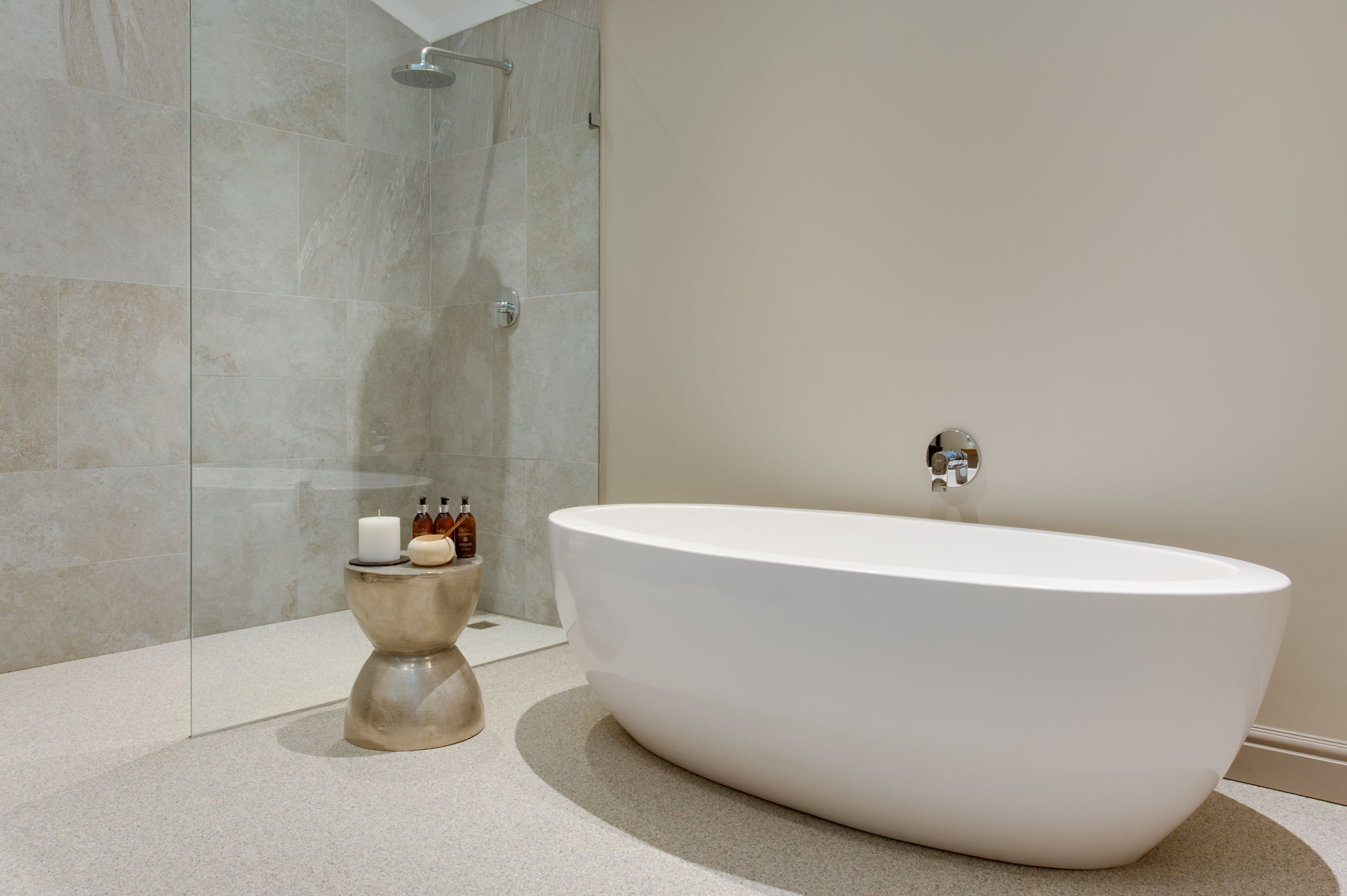 A modern bathroom with a freestanding bathtub, a glass shower enclosure, and a small round table with toiletries.