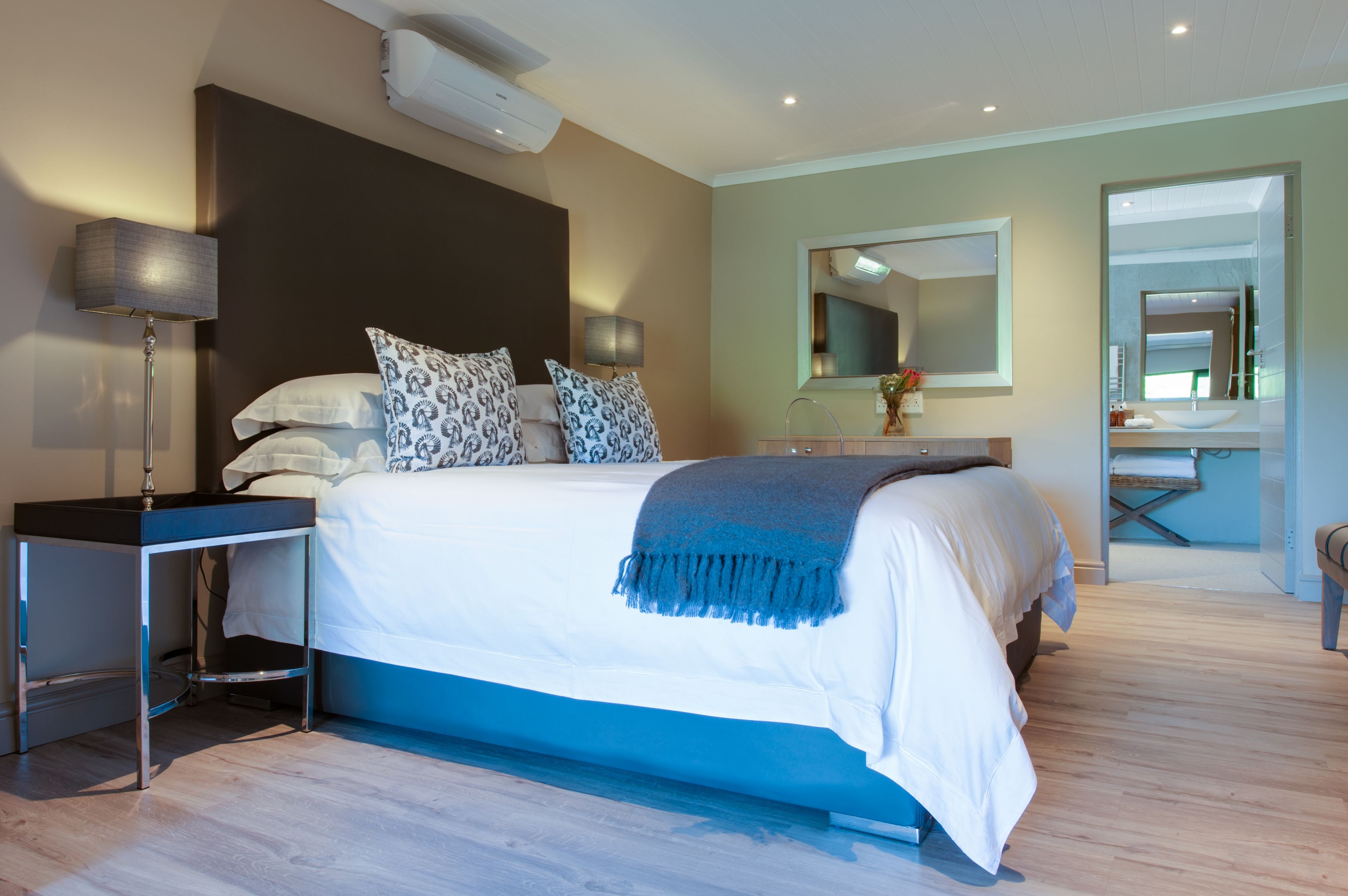 A modern bedroom with a large bed, bedside tables, a mirror, and a bathroom visible through an open door.