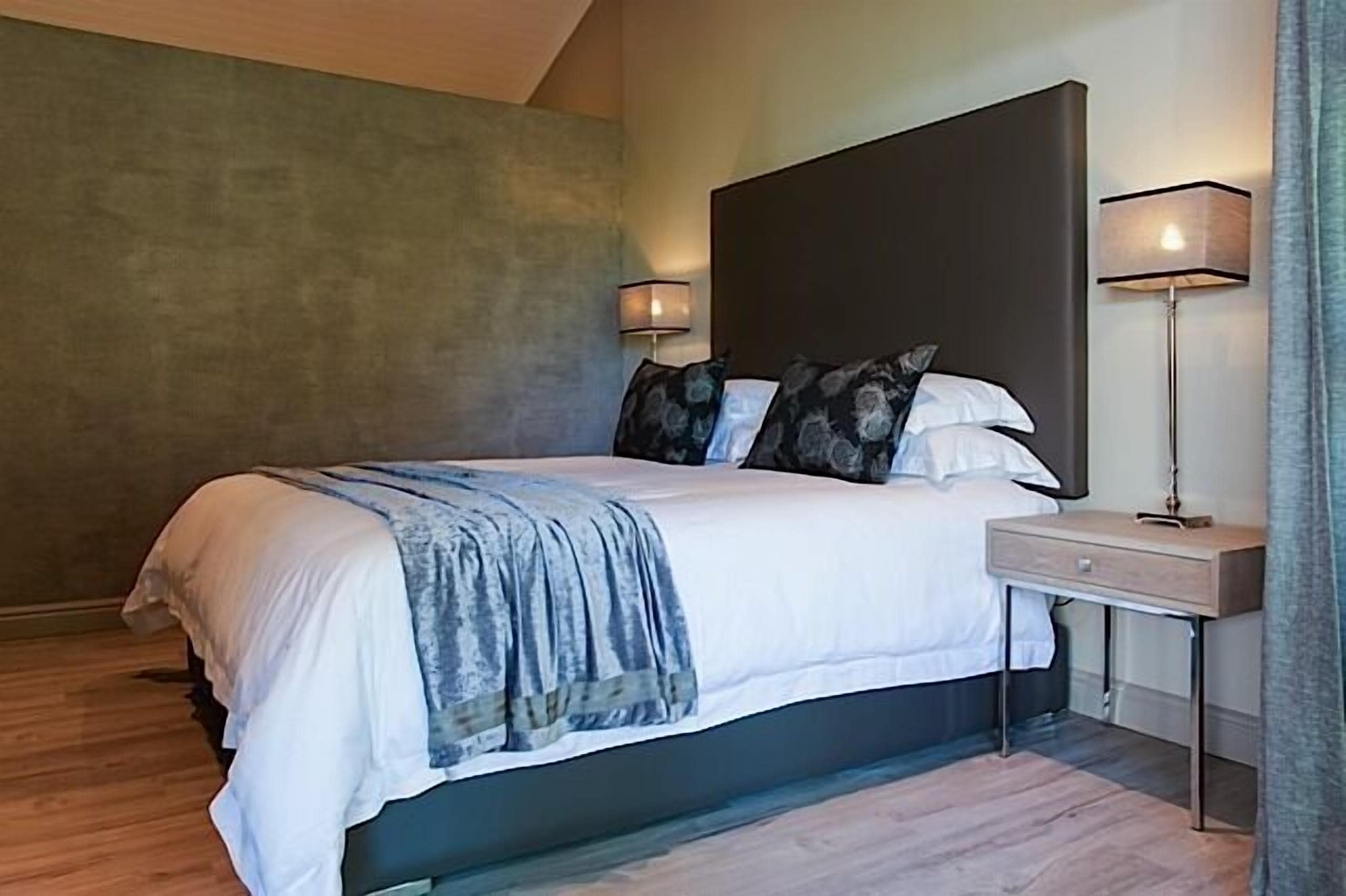 A modern bedroom with a large bed, two bedside lamps, and a nightstand.