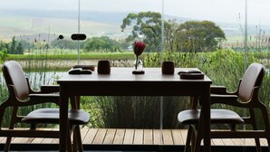 Mesa de jantar com cadeiras num terraço, com vista para uma paisagem com campos e árvores.