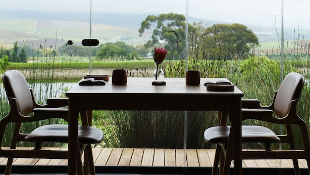 A dining table with chairs on a deck, overlooking a landscape with fields and trees.