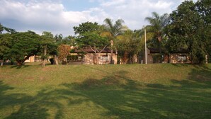 A grassy area with a building that has a tiled roof and a large window. There are trees and a street lamp in the background. - Eagle's Nest Chalets (Hazy view)