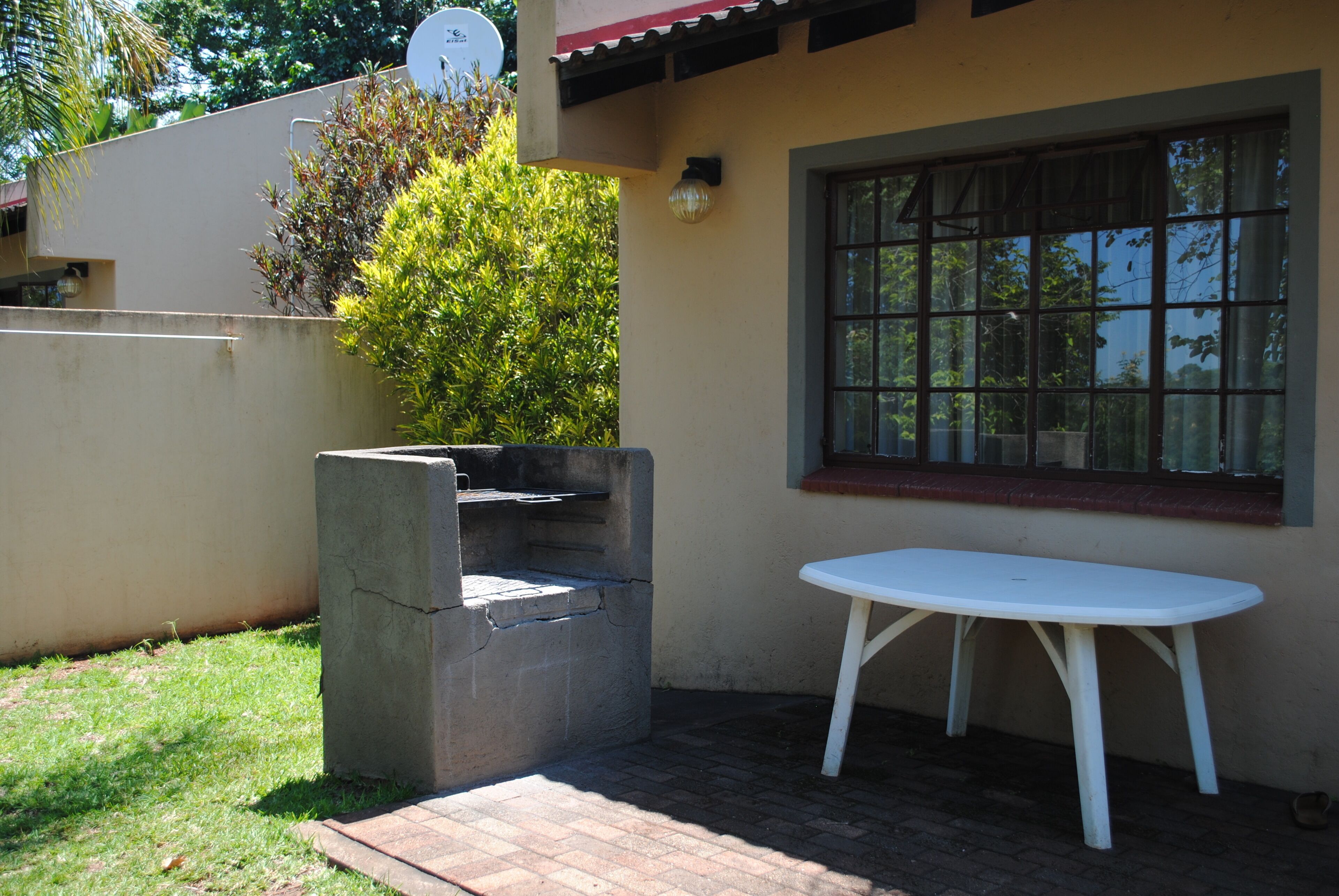 A patio area with a concrete barbecue grill, a white table, and a window with a view of greenery.