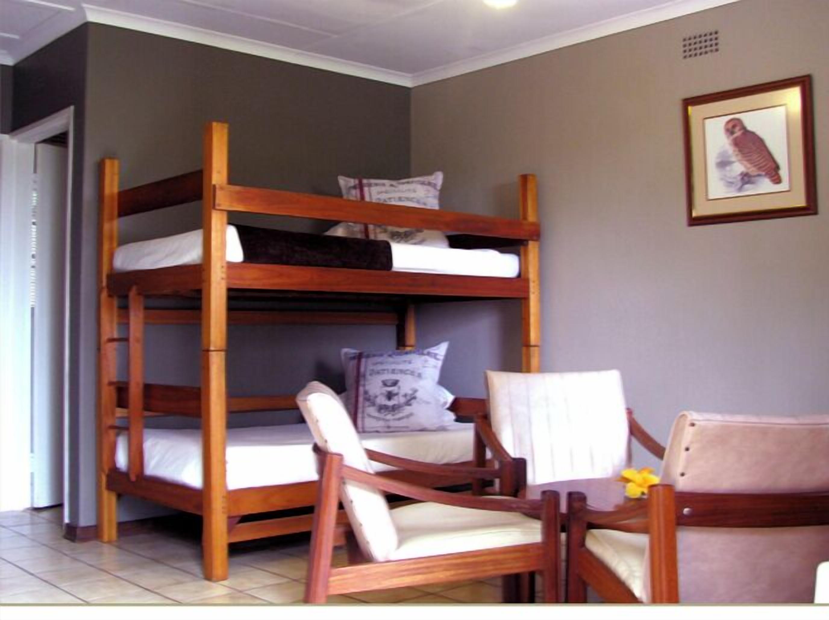 A bunk bed with two wooden chairs, a pillow, and a framed picture on the wall.