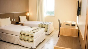 Habitación de hotel con dos camas, un escritorio, una silla, un televisor y una ventana con cortinas.