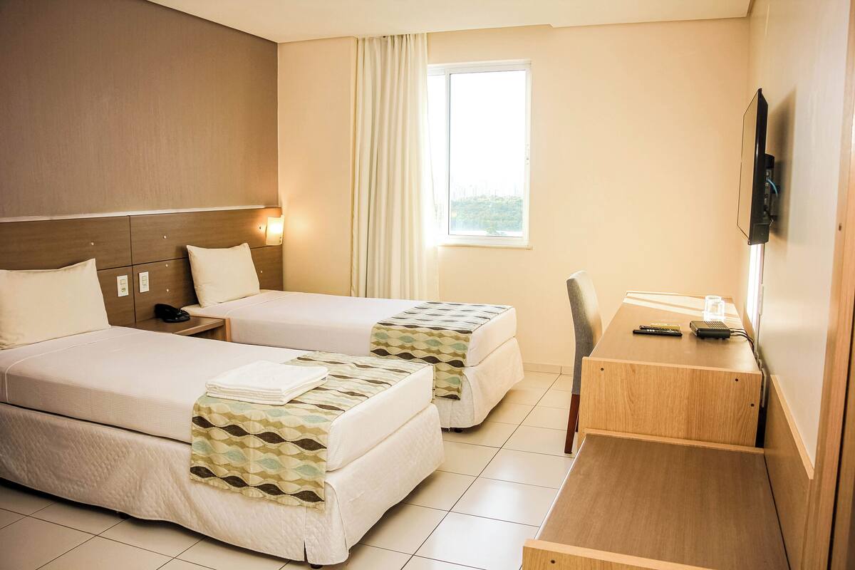 Habitación de hotel con dos camas, un escritorio, una silla, un televisor y una ventana con cortinas.