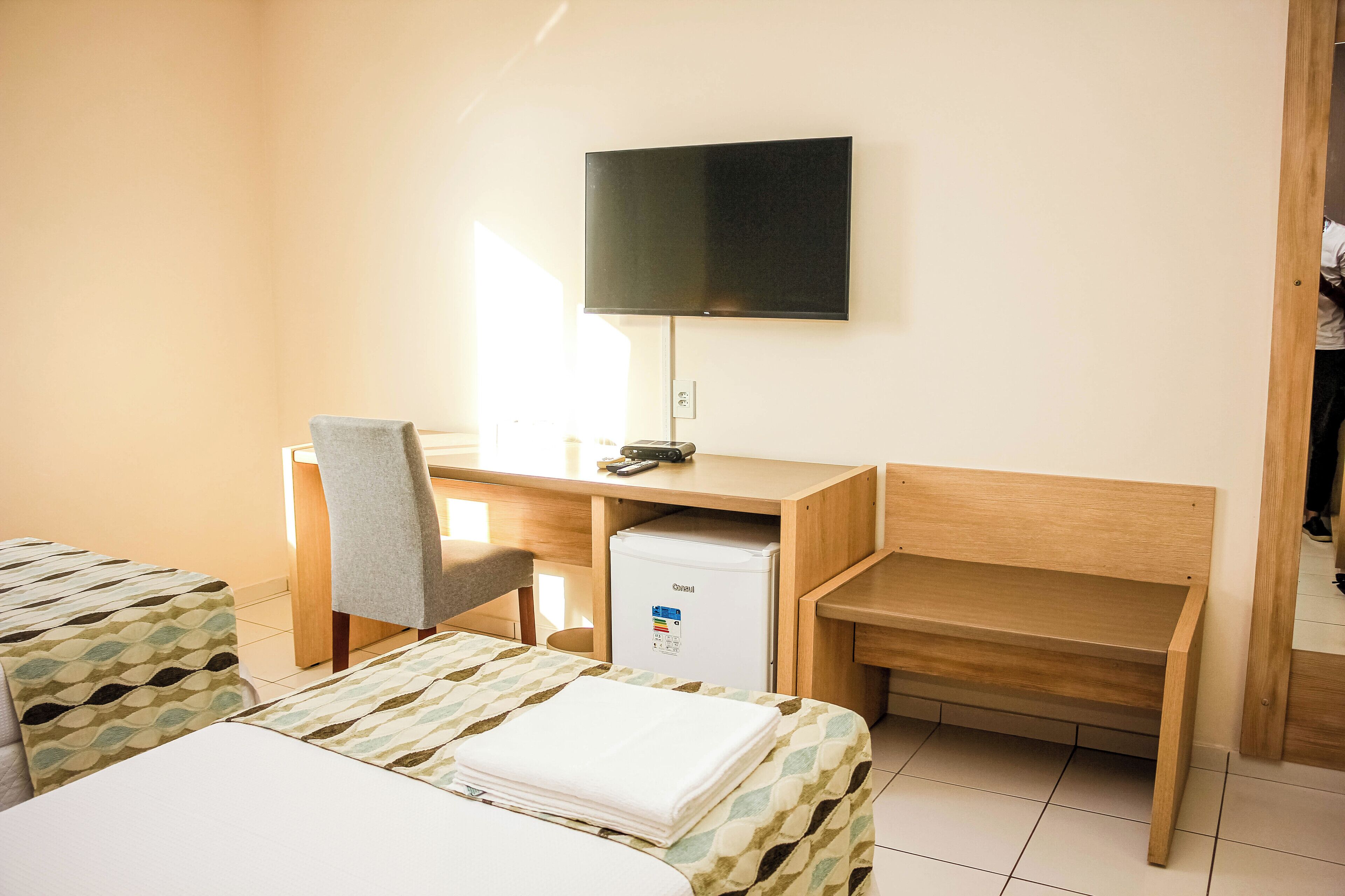 A hotel room with a bed, a desk with a chair, a television, and a small refrigerator.