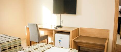 A hotel room with a bed, a desk with a chair, a television, and a small refrigerator.
