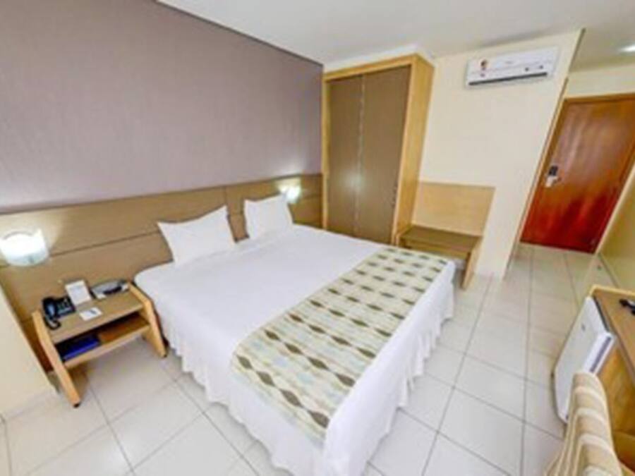 A hotel room with a bed, bedside table, TV, and a wardrobe.