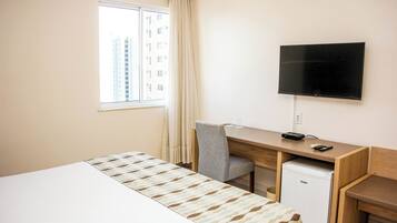 Habitación de hotel con cama, escritorio, computadora, televisor y refrigerador pequeño.