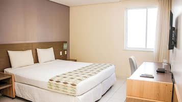 Habitación de hotel con una cama grande, un escritorio, una silla, un televisor y una ventana.