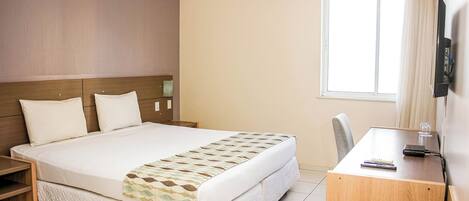 A hotel room with a large bed, a desk, a chair, a TV, and a window.