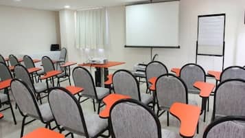 Une salle de conférence avec des rangées de chaises grises dotées d’accoudoirs orange, un projecteur et un écran.
