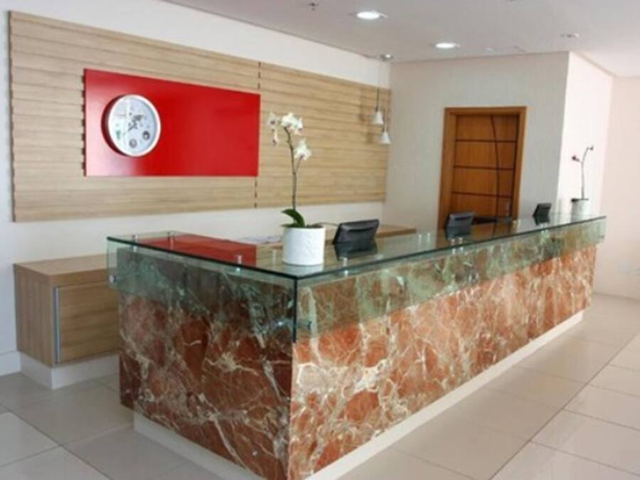 A reception desk with a glass top and marble base, a red clock on the wall, and a wooden panel design.