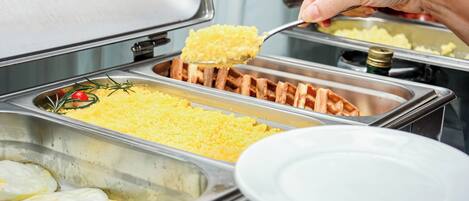 A buffet with various food items including waffles, scrambled eggs, and rice.