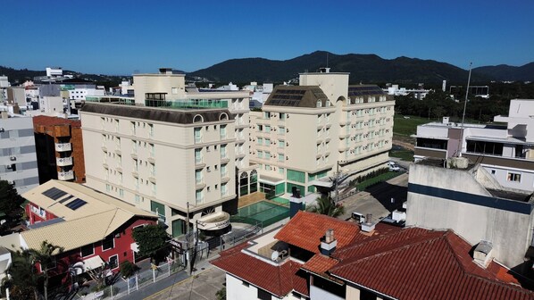 Un hotel de varios pisos con piscina en la azotea, rodeado de otros edificios y con montañas al fondo.