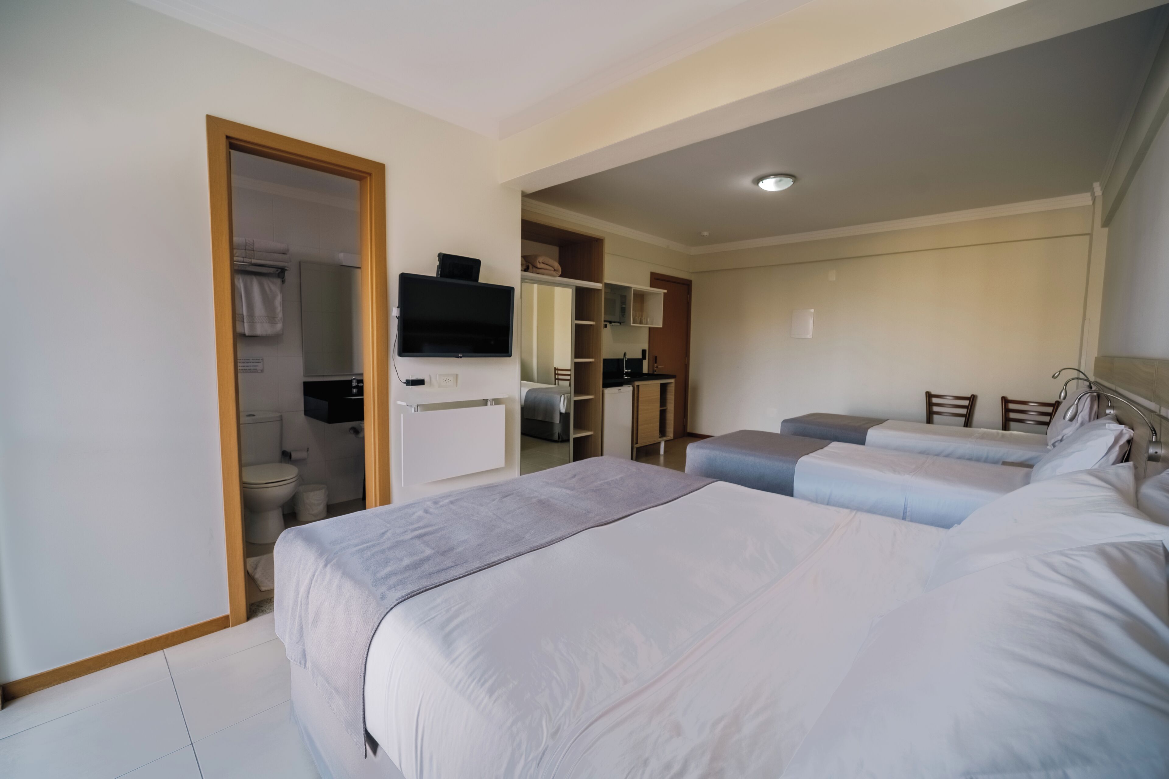 A hotel room with two beds, a bathroom, a kitchenette, and a television.