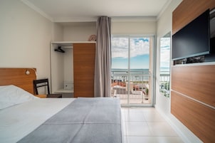 Una camera d'albergo con un letto, una TV a muro, un balcone vista mare e un armadio in legno.
